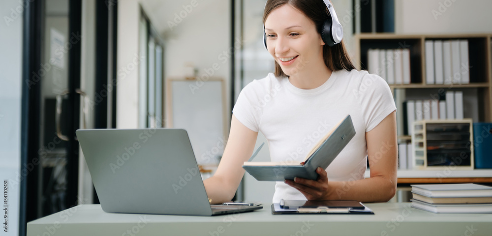 Obraz premium happy young student studying at the college library, sitting at the desk, using a laptop computer, tablet and headphones having a video chat.