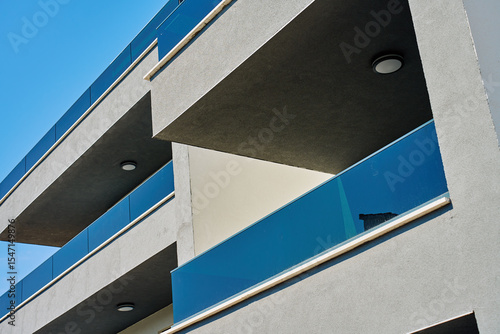 Fotografie Facade of modern apartment building with minimalist balconies and glass railing under blue sky