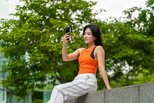 Young Asian woman having a video call on phone in green city park