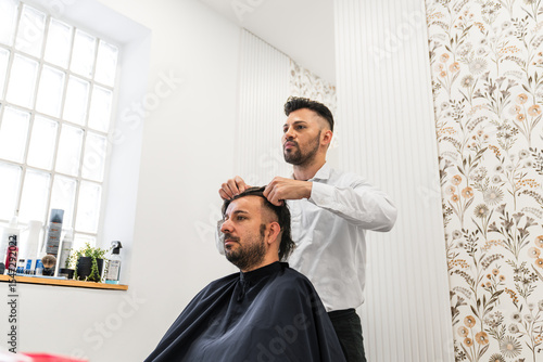 Hairdresser carefully placing hair replacement system on head of male client in hair salon, providing solution for hair loss