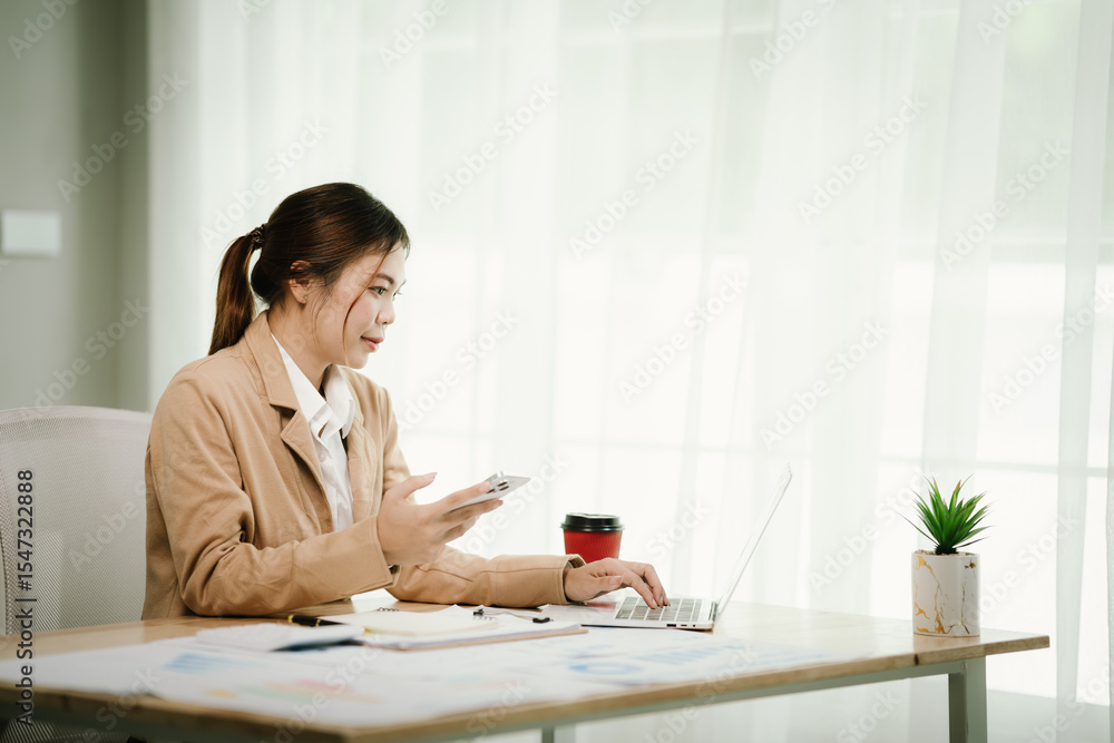 Asian businesswoman working from office with style, determination and self-confidence, using smartphone and laptop to manage tasks, communicate and work efficiently. Asian businesswoman working from office with style, determination and self-confidence, using smartphone and laptop to manage tasks, communicate and work efficiently.