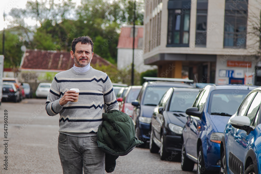 Obraz premium A mature man walks through the city and drinks coffee from a paper cup