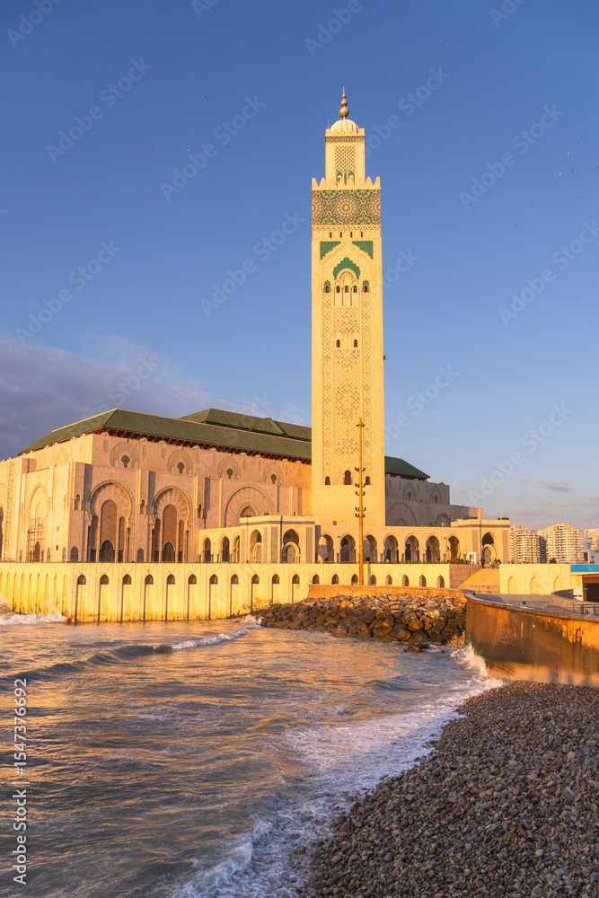 Fototapeta premium Casablanca, Morocco: Sunset over the famous Hassan II mosque and minaret by the Atlantic ocean in Casablanca, Morocco largest city.