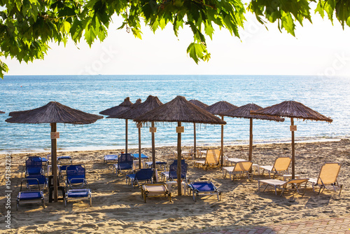 Fototapeta Naklejka Na Ścianę i Meble -  Row of wooden umbrellas at sandy beach, sea during the sunset