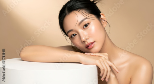 깨끗하고 빛나는 피부를 가진 아름다운 아시아 여성이 스킨케어 제품 디스플레이를 위해 흰색 원형 받침대에 기대어 있는 이미지