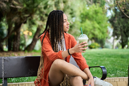 Canvas Print Young latina woman with braids enjoying a refreshing drink in the park
