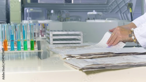 Medical professional or scientist organizes patient test results and paperwork in a modern clinical laboratory with colorful chemical samples in test tubes.