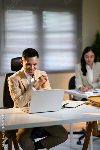 Smiling businessman enjoying coffee while working on laptop at office desk