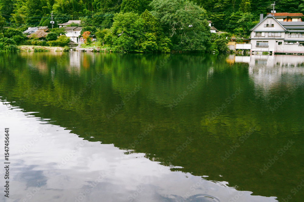 Fototapeta premium Calm Lake Reflecting Buildings and Greenery. Peaceful Reflections on Lake with Lakeside Architecture.