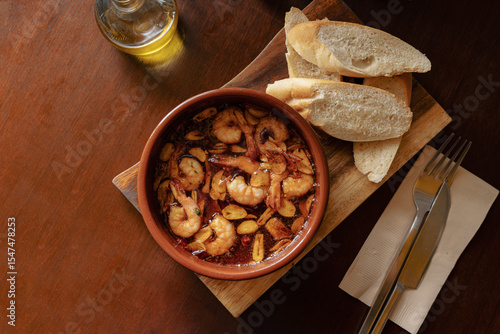 Spanish Gambas al Ajillo with Garlic and Olive Oil, Served with Baguette and Cutlery on Wooden Table