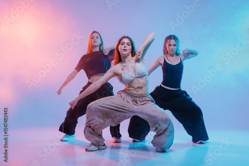 Obraz na płótnie Three Young Women Performing Jazz Funk Dance in Studio with Colorful Lighting an