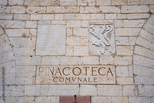 Stone-carved sign of the Pinacoteca Comunale art gallery at Palazzo Vallemani in the medieval historic center of Assisi, Umbria, Italy.