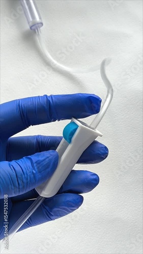 A woman's hand in a medical glove holds an infusion system on a white background. The doctor regulates the rate of administration of the solution. Intravenous infusion of medication.