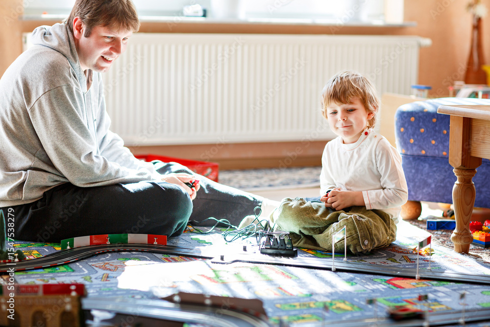 Fototapeta premium Father and son playing with racing cars on racetrack, indoors, with cars. Happy little preschool boy and young man having fun with indoor race game