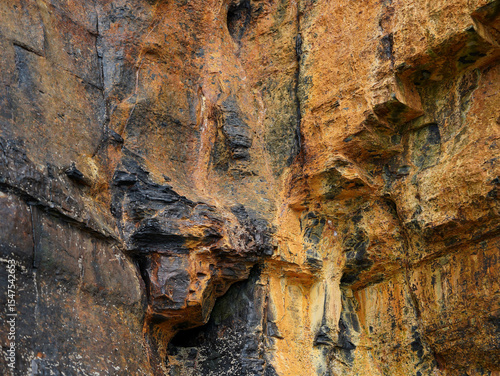 The rugged rock face is covered with orange, yellow, and black mineral streaks