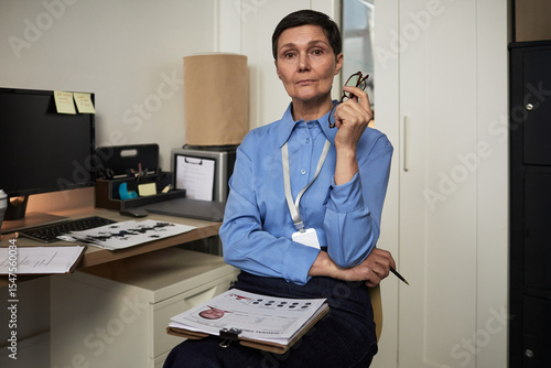 Fototapeta Portrait of middle aged Caucasian woman sitting in office holding eyeglasses and
