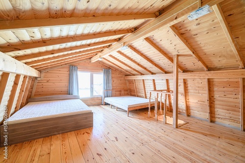 rustic room features exposed wooden beams and walls. Two beds are present, one against a window, creating a cozy, natural space