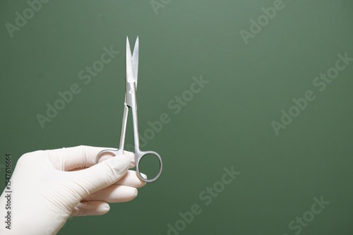 Gloved Hand Holding Surgical Scissors Against Green Background