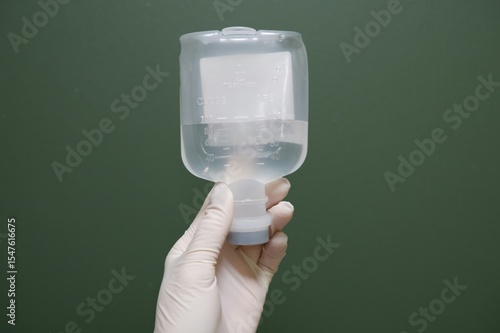 Gloved Hand Holding Intravenous Fluid Bag Against Green Background