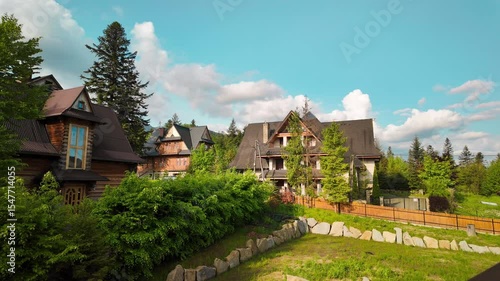 Wallpaper Mural Charming wooden houses with steep roofs line a quiet village street in a mountain area. Surrounded by green trees and a blue sky with clouds, the scene radiates peacefulness and alpine charm. Torontodigital.ca