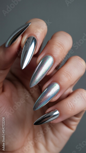 Close-up of long, pointed, silver nails with a chrome finish.
