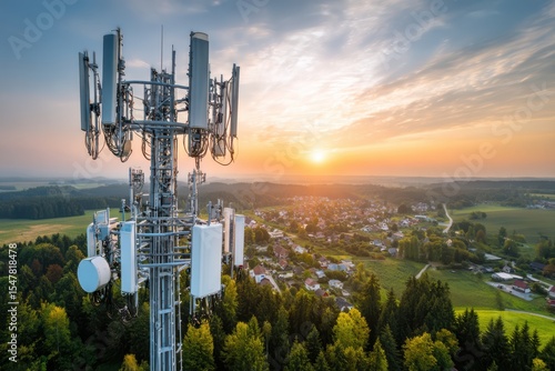 A 5G cell tower in a rural landscape providing fast internet access. The tower stands tall against the clear blue sky, surrounded by green fields and trees.