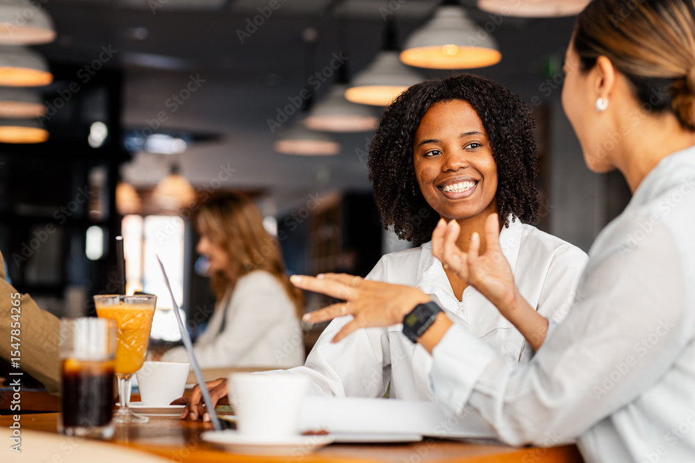Hispanic woman and coworker talking about work while using laptop in modern coffee shop. Hispanic woman and coworker talking about work while using laptop in modern coffee shop.
