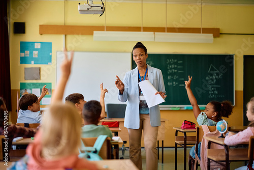 African American elementary school teacher pointing at student with raised arm who wants to answer question.