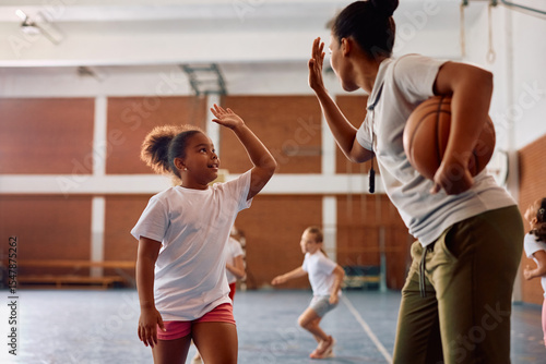 Fototapeta Naklejka Na Ścianę i Meble -  Happy black schoolgirl and her sports teacher giving high-five during PE class.