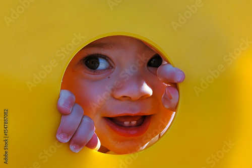 Photos Smiling Toddler Peeking Through a Yellow Playground Circle