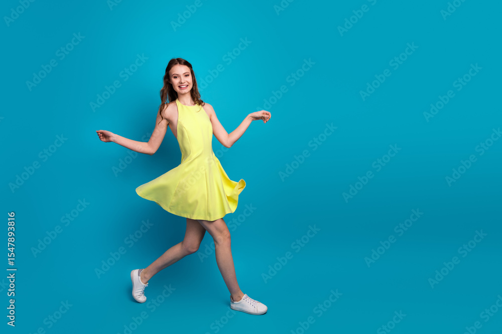 Obraz premium Fashionable young woman in a vibrant yellow dress showcasing style and elegance against a bright blue background