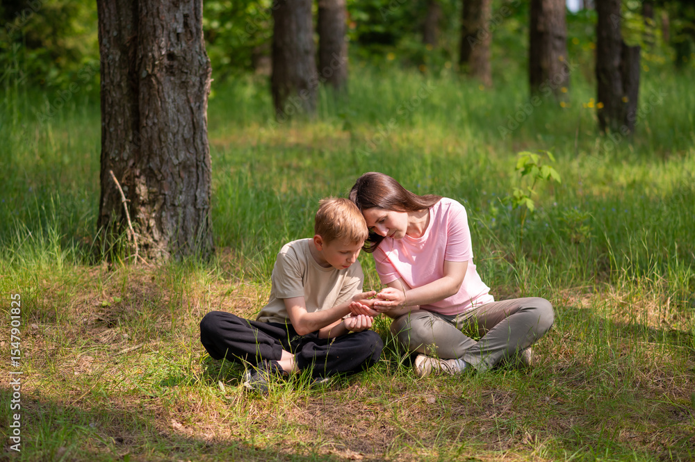 Fototapeta premium mother and son are sitting side by side in a forest clearing and looking at something in their palms