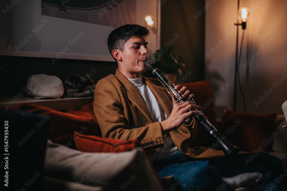 Fototapeta premium A man in a warm-toned room is playing a clarinet, focusing passionately on his music. The setting appears intimate and comfortable, suggesting a mood of relaxation and musical expression.