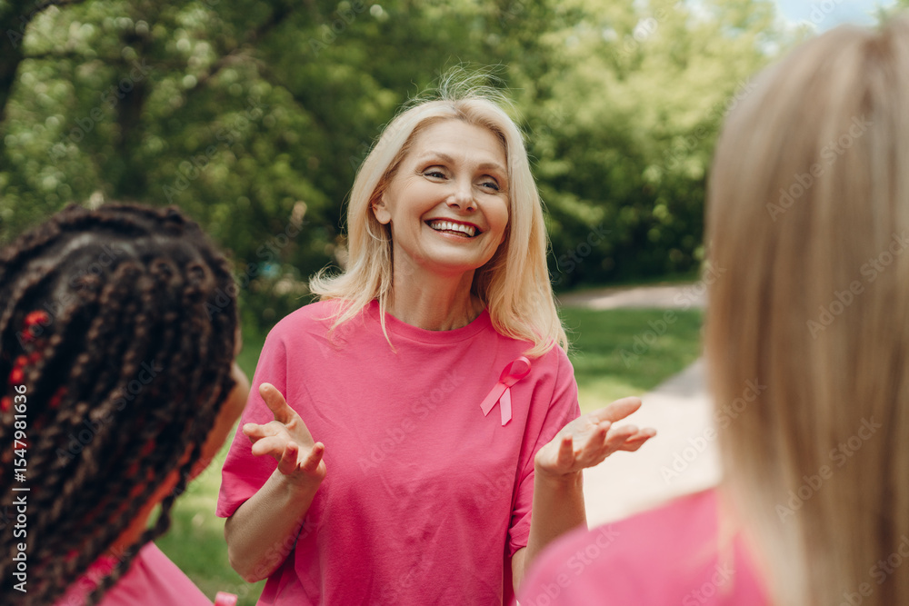 Fototapeta premium Smiling mature woman supporting breast cancer awareness campaign talking to volunteers in park