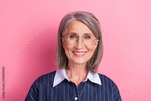 Portrait of a confident woman with glasses smiling against a pink background wearing a casual striped blouse