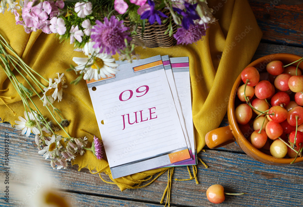 Naklejka premium Calendar for July 9: flip calendar with numbers 09, name of the month July in English on a yellow napkin with wild flowers and ripe cherries