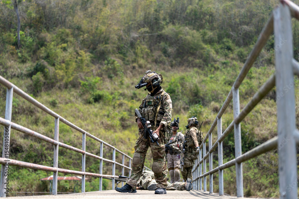 Tactical military team securing a bridge during field operation with soldier laying on ground and team coordination in action. Tactical military team securing a bridge during field operation with soldier laying on ground and team coordination in action.