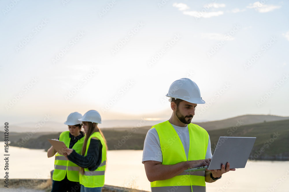 Engineers working with laptop and tablet near a lake at sunset promoting technical careers Engineers working with laptop and tablet near a lake at sunset promoting technical careers