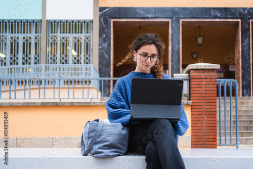 Focused student using digital tablet for online learning, enjoying fresh air and modern campus facilities