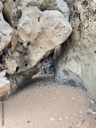 Coastal Cave: An evocative composition of weathered rocks, shaped by the sea's embrace, framing a shadowed cavern entrance and textured sand