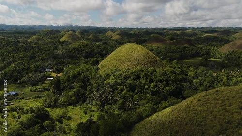 A lone majestic Chocolate Hill emerges from a thick green forest Among Dense Jungle in sunny cloudy day, Bohol, Philippines