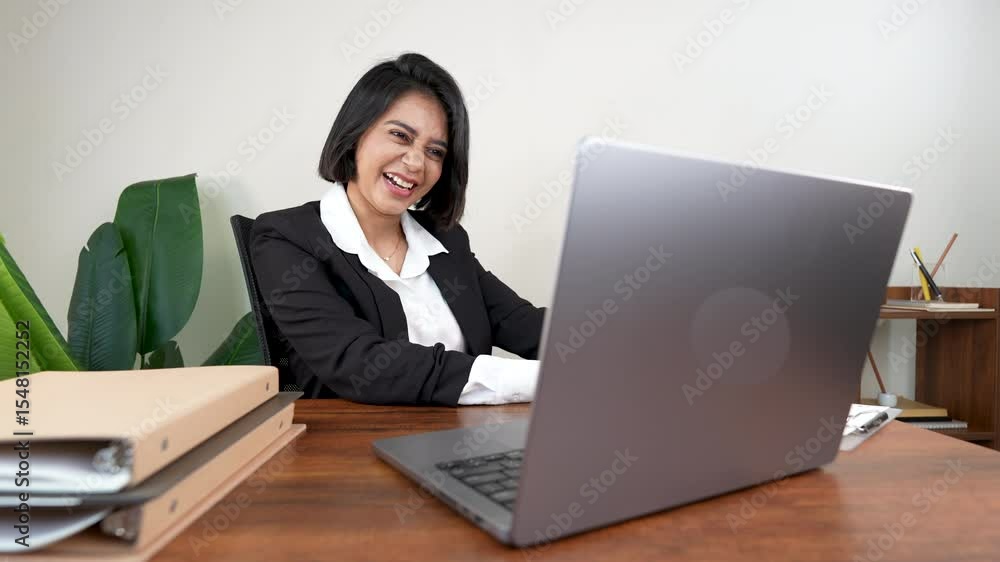 Cheerful woman with short dark hair laughs heartily while looking at her laptop at a wooden desk Cheerful woman with short dark hair laughs heartily while looking at her laptop at a wooden desk