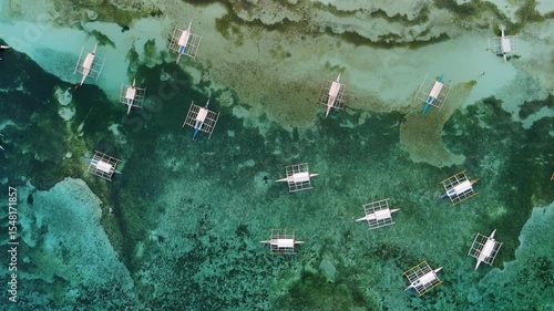 Bird's eye top aerial view of multiple Bangka Boats Floating in Surreal Coastal Waters near the shore of Alona Beach and White beach in Panglao Island, Bohol, Philippines