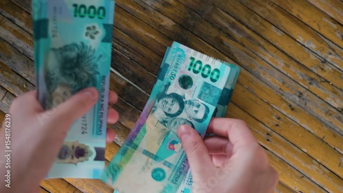 Close-up of a Person Holding and Counting New Philippine 1000 Peso Polymer Banknotes Over a Rustic Wooden Table Surface – Featuring Hands, Currency Security Details, and Filipino Historical Figures