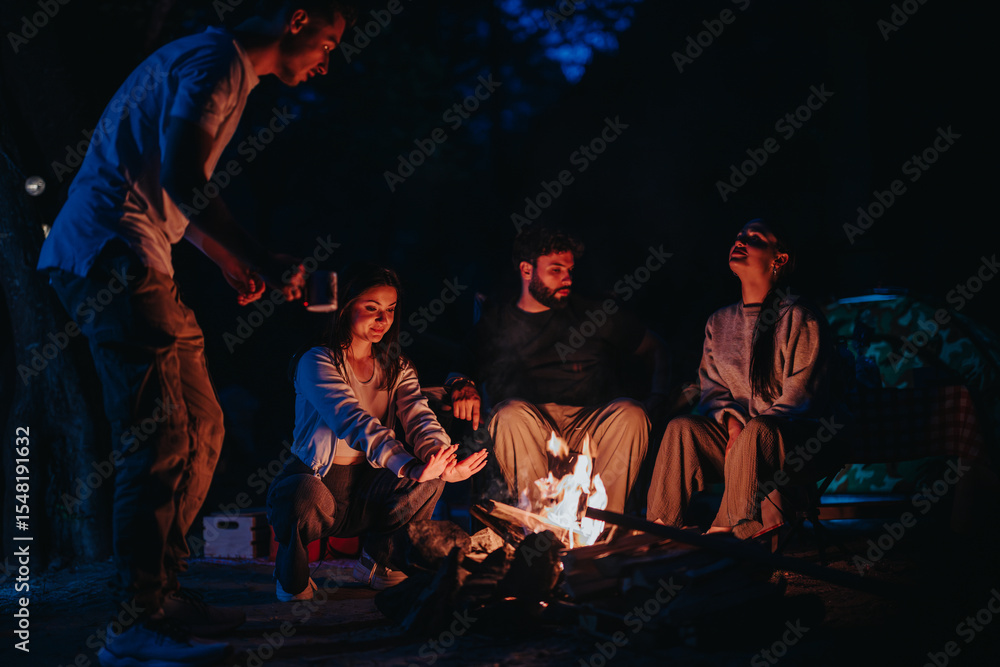 Obraz premium A group of friends relaxing around a campfire in the evening, enjoying warmth and camaraderie in an outdoor setting beneath a dark, starry sky.