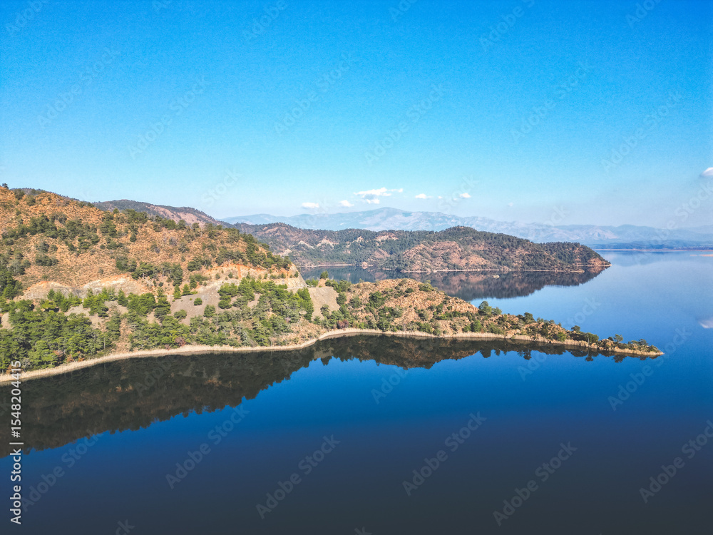 Obraz premium Lush green mountain reflected in clear water. Vibrant natural landscape with rich vegetation and a calm lake or river at the base of the hill.