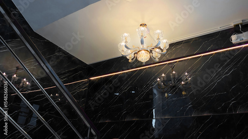 Elegant Crystal Chandelier Illuminating a Modern Luxury Staircase with Black Marble Wall and Stainless Steel Railing
