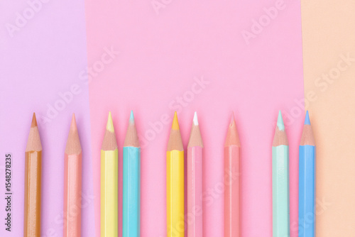 Pastel colored pencils arranged in a row on pink and peach background. Minimalist flat lay, creative art supplies, back to school, education, stationery, and design concept.

