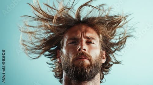A man with wild, flowing hair stares intensely into the camera, capturing a vibrant and dynamic expression against an artistic blue background, evoking emotion and intrigue.