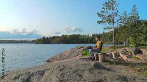 The man comes up, sits on a bench on the stone shore lake and looks into the distance. The concept of reflection, loneliness, solitude, travel. Normal speed.